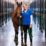 A brown horse being handled by a happy female trainer inside a facility