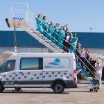 A group of people standing on airstairs behind a white pet transportation van